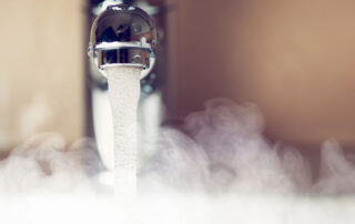 Hot water flowing from a modern faucet with steam rising, representing energy-efficient water heating.